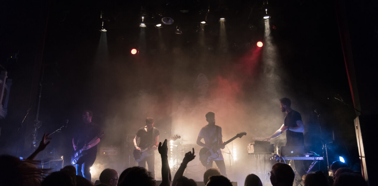 View from the back of the stalls of a cheering crowd and a band on stage.