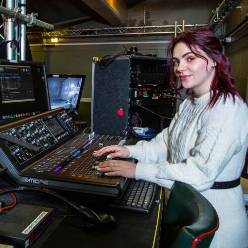 A young woman operating the theatre sound desk