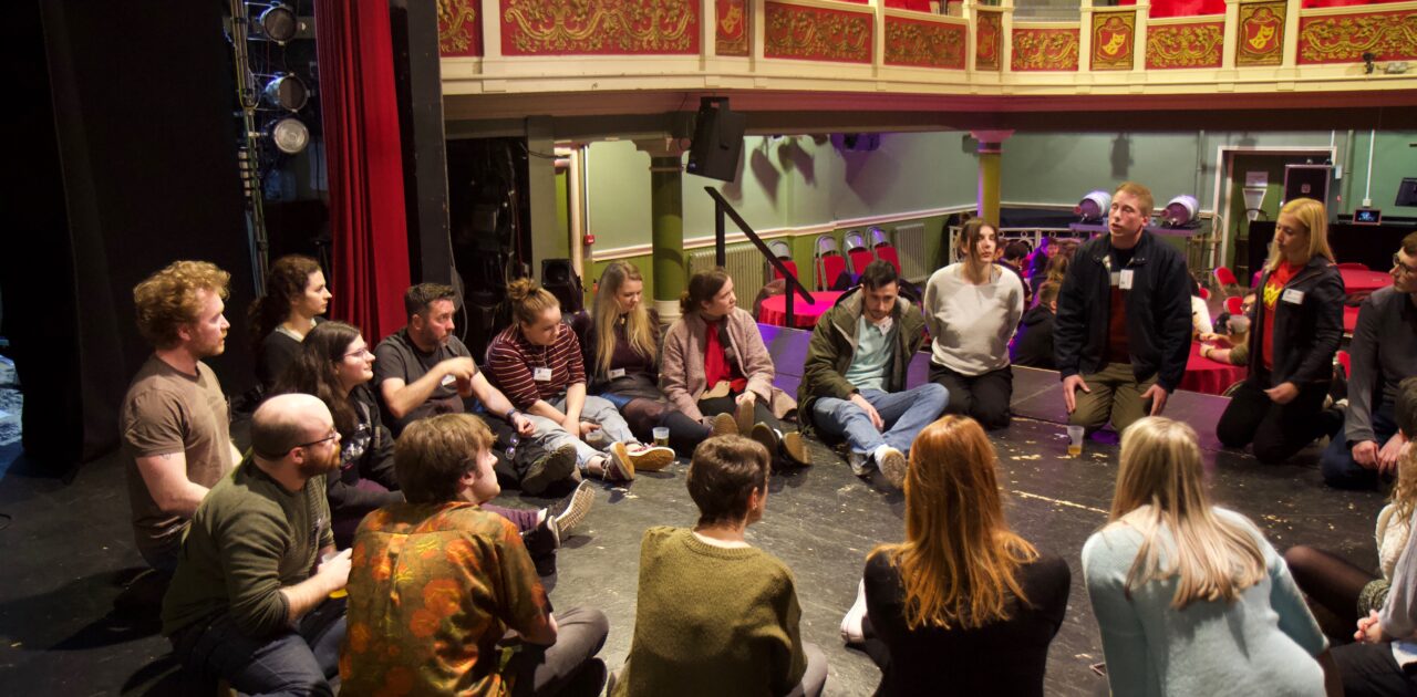 A circle of people on the theatr stage having a discussion