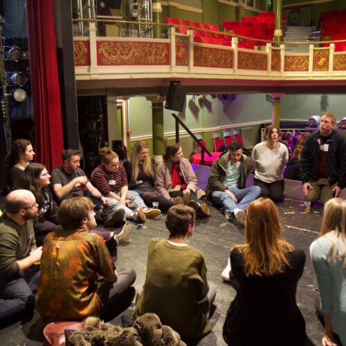 A circle of people on the theatr stage having a discussion