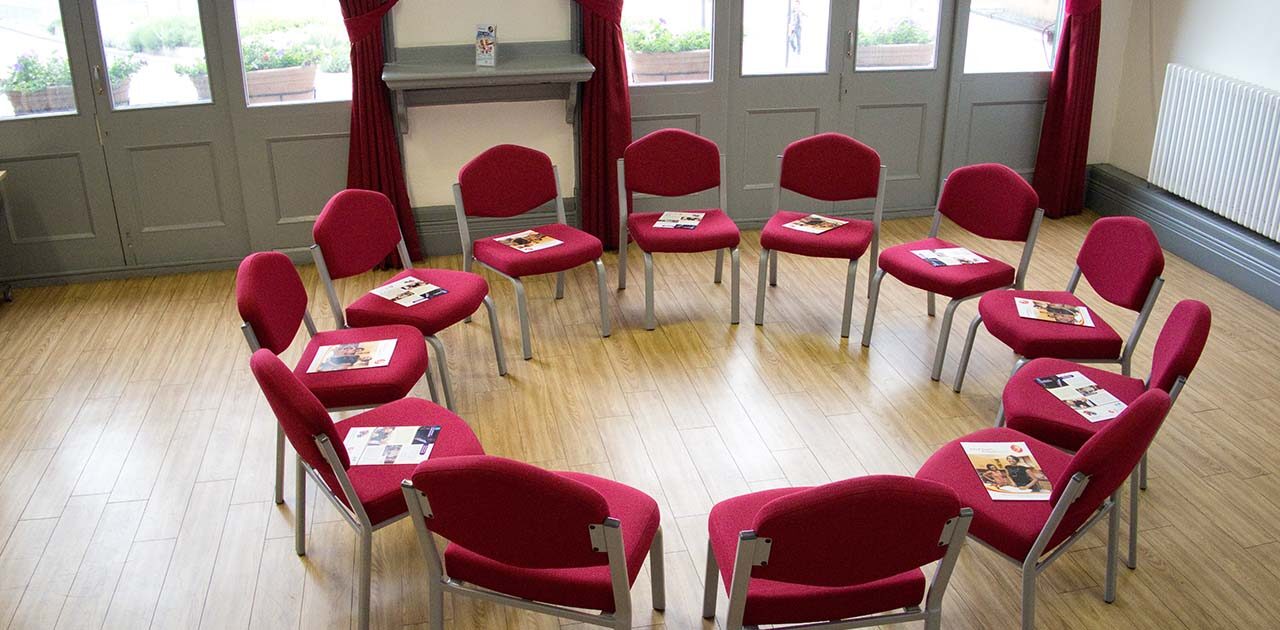 The Percy Barratt room with chairs in a circle, each with a leaflet on, with the large windows behind.