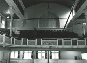The Y Theatre before the bar was added, with windows at the back of the auditorium and the high chuch-like window. A blurry man (or ghost!) walks among the balcony seats.