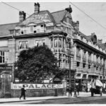 A black and white photo of the YMCA building, a sign outside reads "To the Palace"