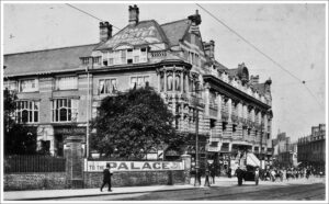 A black and white photo of the YMCA building, a sign outside reads "To the Palace"